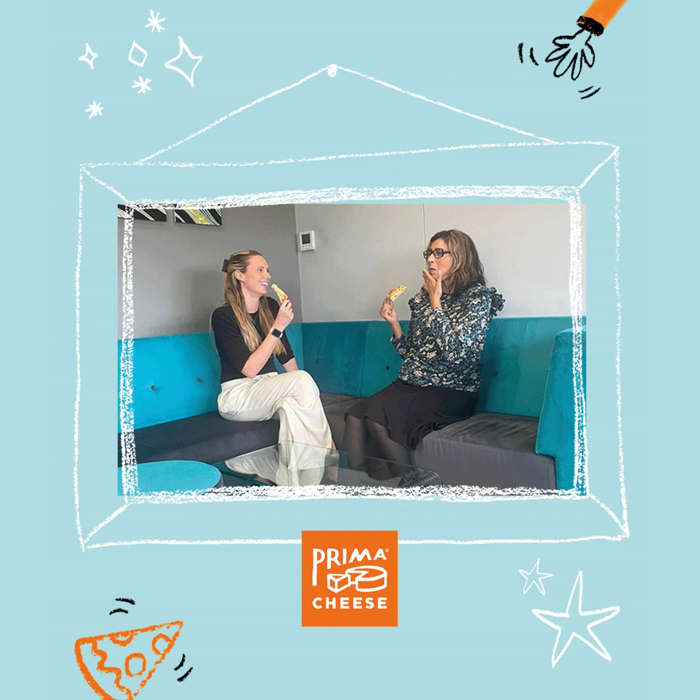 Two female staff members sit on a blue sofa happily enjoying a slice of free pizza.